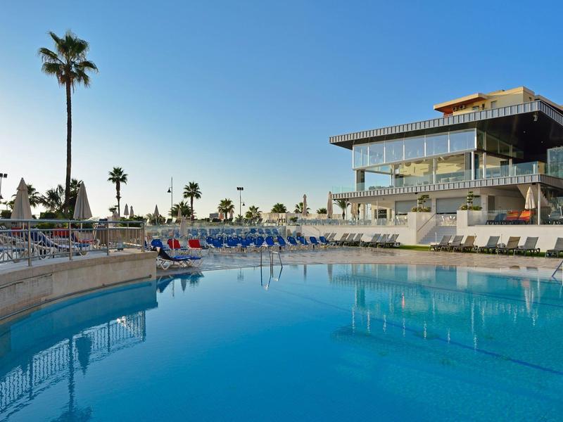 Velký modrý bazén s palmami a moderní hotelová budova za soumraku.