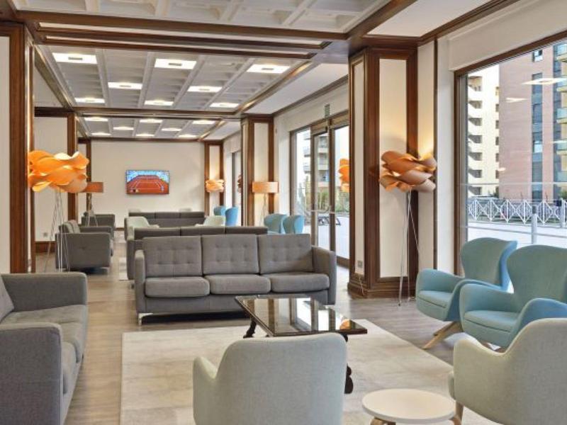 Moderní hotelový lounge s barevnými pohovkami a křesly, velkými okny a městským výhledem.