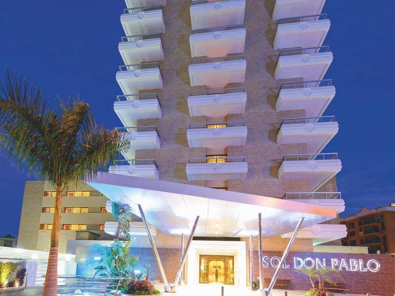 Moderní hotel s osvětlenou fasádou na pozadí noční modré oblohy.