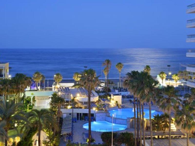 Noční pohled na hotelový komplex s bazénem a palmami u moře.