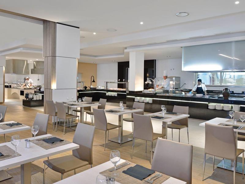 Moderní hotelová jídelna s elegantními stoly a otevřenou kuchyní.