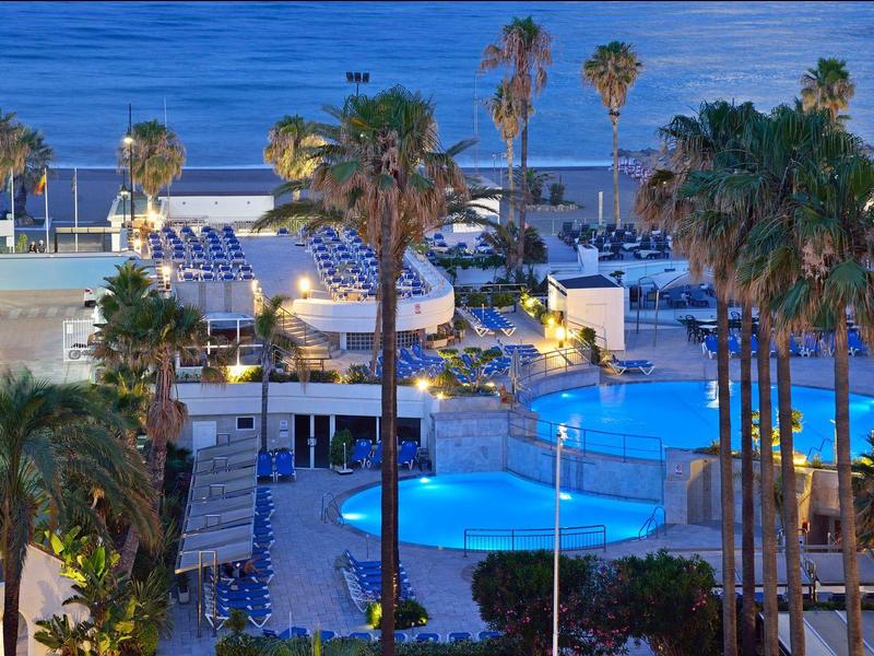 Noční osvětlený bazén obklopený palmami v přímořském hotelu.