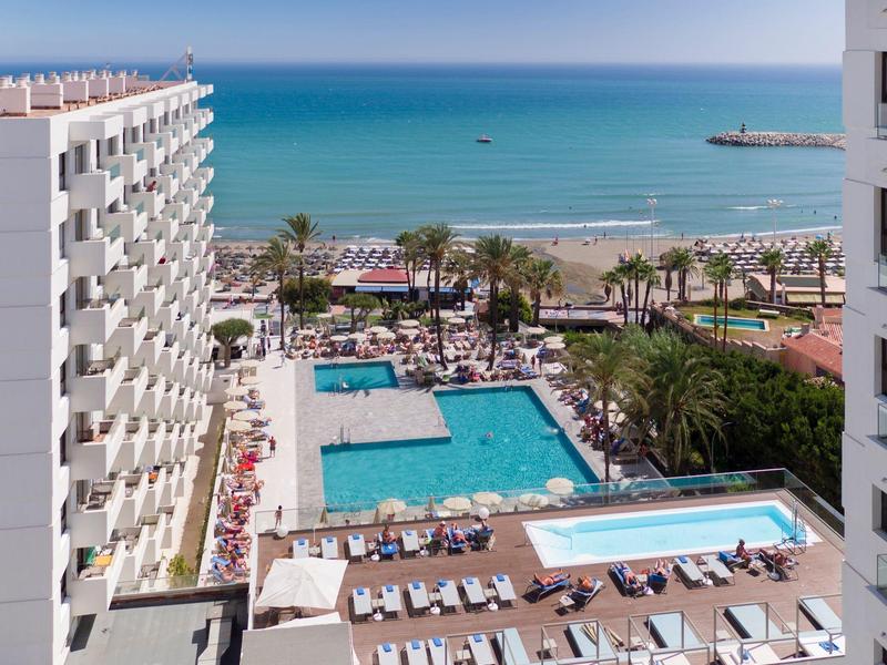 Vue d'un hôtel avec piscines, transats et vue sur la mer au bord d'une plage.