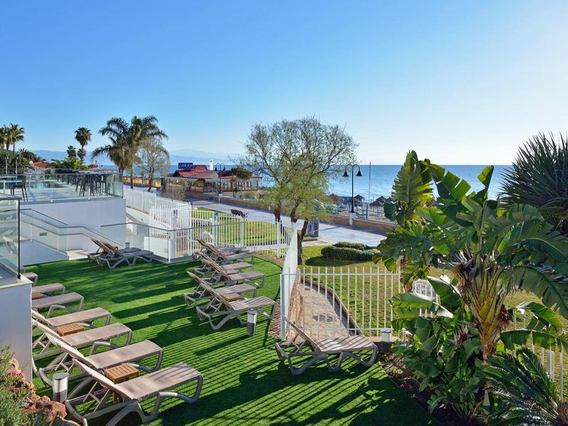 Jardin avec chaises longues face à la mer sous un ciel dégagé.