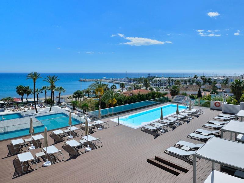 Piscines extérieures avec chaises longues et vue sur la mer sous un ciel bleu clair.