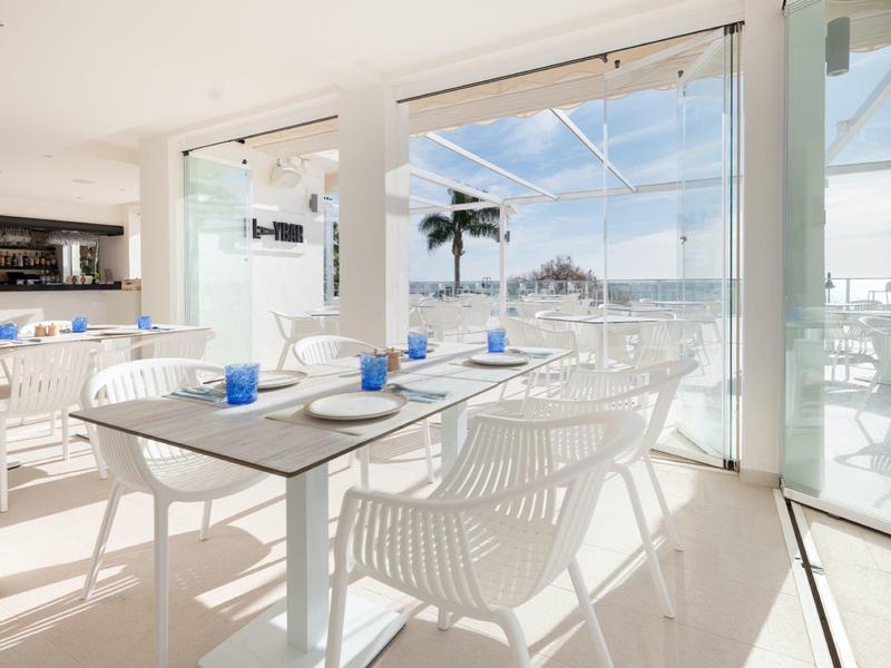 Salle à manger lumineuse avec vue sur une plage et mobilier blanc moderne.