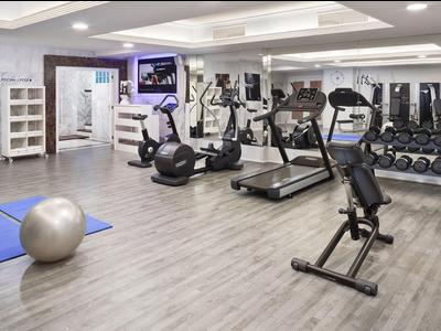 Gimnasio moderno con cinta de correr, pesas y esterillas sobre suelo de madera clara.