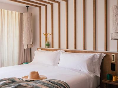 Lichte hotelkamer met groot bed, wit beddengoed, houten accenten en een hoed op de deken.