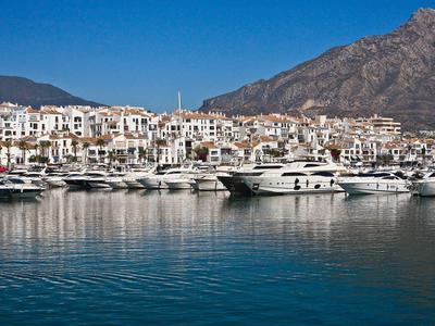 Jachthaven met luxe boten voor een kustplaats en bergen op de achtergrond.