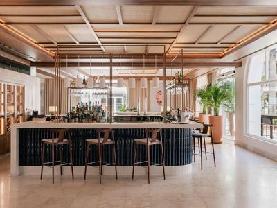 Moderne hotel loungeruimte met bar, barkrukken en grote ramen die natuurlijk licht binnenlaten.