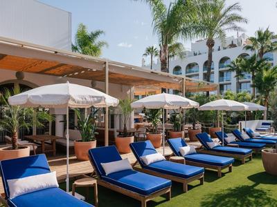 Blauwe ligstoelen met witte kussens onder witte parasols naast een hotel met palmbomen.