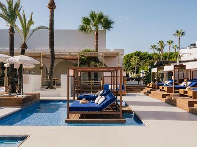 Área de piscina moderna con tumbonas azules y palmeras en un hotel.