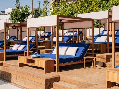 Luxe strandbedden met blauwe kussens en houten tafels op een houten buitendek.
