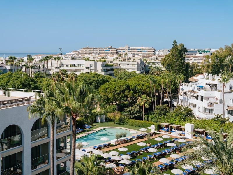 Hotelcomplex met zwembaden, ligstoelen en palmbomen onder een blauwe lucht