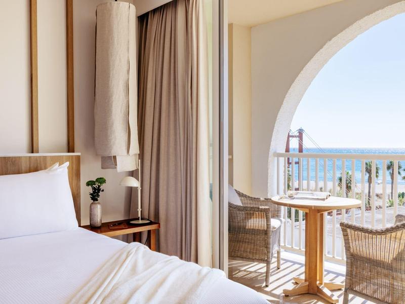 Lichte hotelkamer met groot bed en balkon met zeezicht en zithoek.