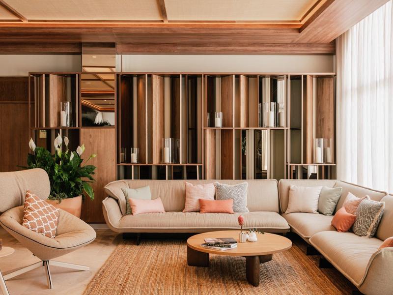 Moderne woonkamer met beige banken, houten planken en grote ramen met witte gordijnen.