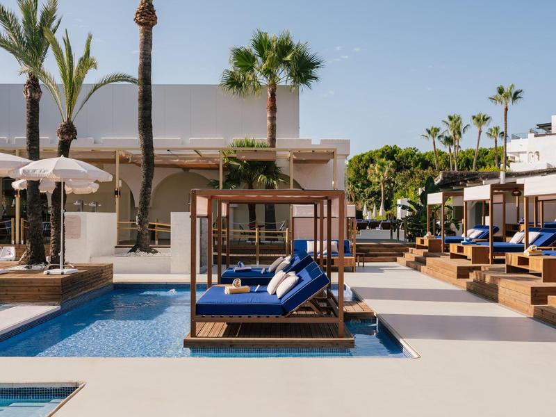 Moderne zwembadruimte met blauwe ligbedden en palmbomen bij een hotelresort.