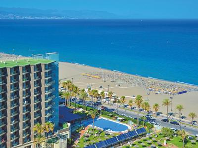 Moderní hotelový komplex s bazénem vedle široké písečné pláže a modrého moře.