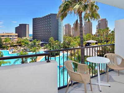 Balkon s židlemi a stolem s výhledem na hotelový bazén a město v pozadí.