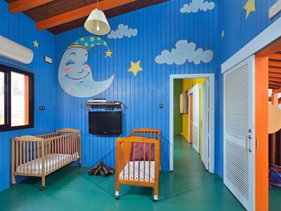 Dětský pokoj s modrými stěnami s motivem měsíce a hvězd, dvě kolébky a televize.