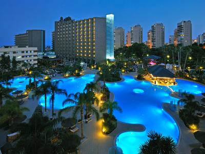 Hotelkomplex bei Nacht mit beleuchtetem Pool und hohen Gebäuden im Hintergrund.