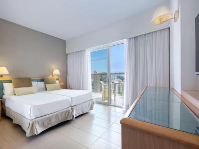 Světle hotelový pokoj s manželskou postelí, terasou a moderním nábytkem.