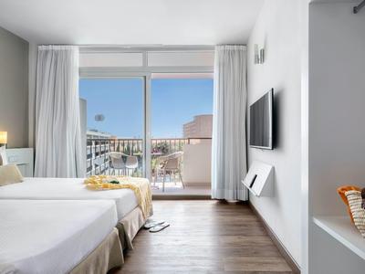 Jasný hotelový pokoj s manželskou postelí a balkonem s výhledem na město.