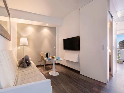 Moderní obývací část hotelového pokoje s pohovkou, TV a malým stolem.