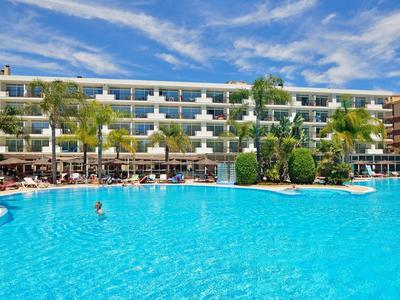 Velký hotel s velkým modrým bazénem a slunečními deštníky pod jasně modrou oblohou