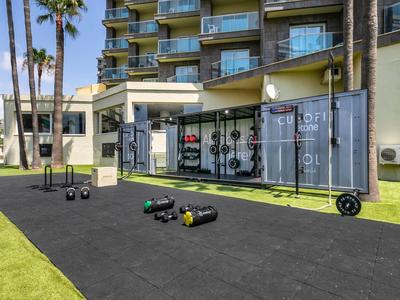 Outdoor-Fitnessbereich mit Gewichten und Boxsack vor einem Hotelgebäude und Palmen