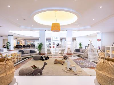 Heller, moderner Hotelspielraum mit Teppichen, Kissen, Spielzeug und Loungemöbeln.