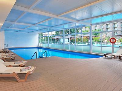 Vnitřní bazén s několika lehátky a velkými okny s výhledem na venkovní prostor.