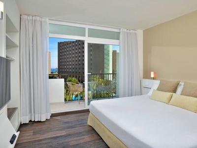 Helles Hotelzimmer mit großem Bett und Balkon mit Stadtblick.