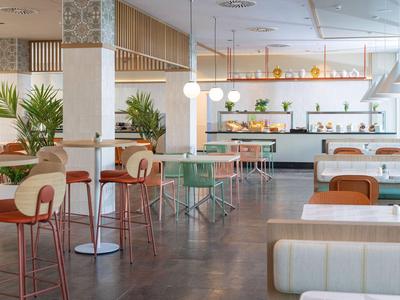Modernes Hotelrestaurant mit hellem Interieur, Pflanzen und verschiedenen Sitzbereichen.