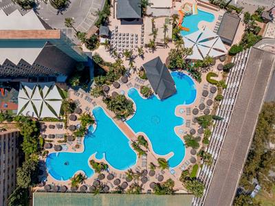 Großer Hotelpool mit geschwungener Form und umliegenden Liegen und Sonnenschirmen.