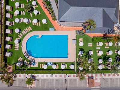 Vogelperspektive auf einen rechteckigen Pool mit Liegestühlen und Sonnenschirmen im Hotelgarten.