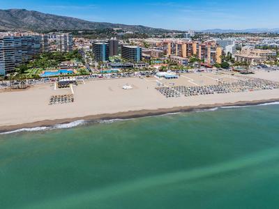 Großer Sandstrand mit Sonnenschirmen und Hotels im Hintergrund unter klarem Himmel.