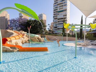 Kinderbereich eines Hotels mit flachem Pool, Wasserspielen und Rutsche im Freien.