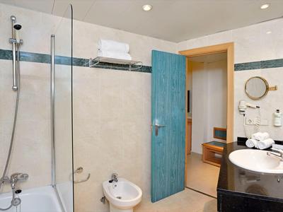 Moderní koupelna s vanou, bidetem, umyvadlem a otevřenými modrými dveřmi.