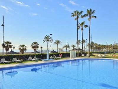 Modrý bazén s lehátky, palmami a modrou oblohou u moře.