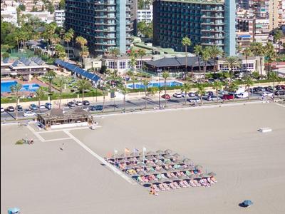 Velký hotelový komplex s bazény a pláží přímo u moře, obklopený městem a kopci.