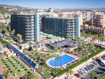 Velký hotel s bazénem, palmami a lehátky ve slunném přímořském městě.