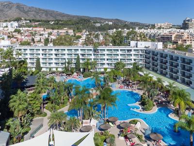 Velký hotel s několika bazény, obklopený palmami a horami v pozadí.