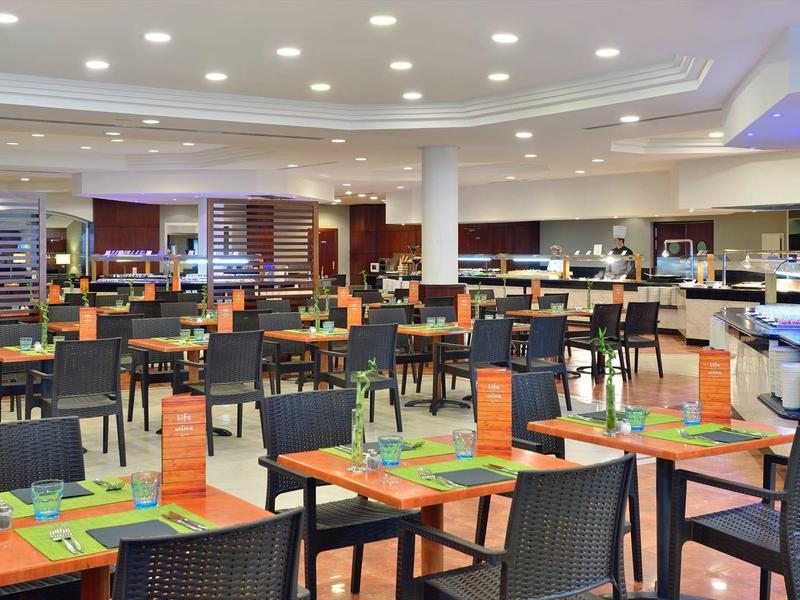 Moderní velká restaurace s mnoha stoly a židlemi, jasně osvětlená.