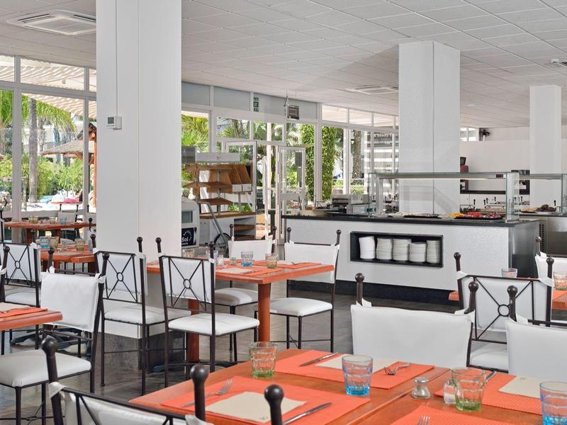 Moderní restaurace s oranžovými ubrusy a bílými židlemi s černými rámy.