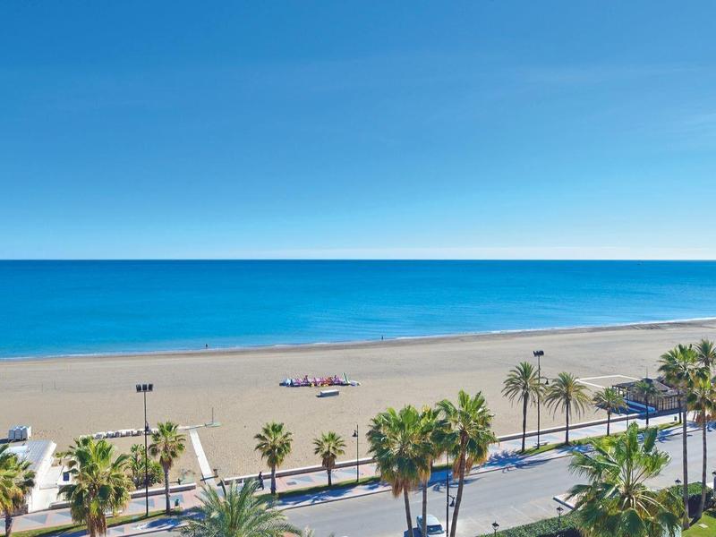 Pláž s palmami a silnicemi podél pobřeží pod modrou oblohou.