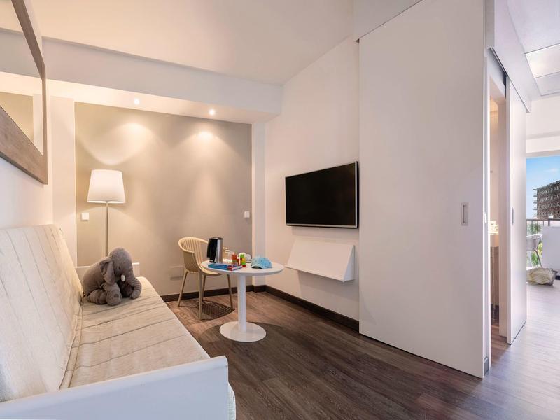 Moderní obývací část hotelového pokoje s pohovkou, TV a malým stolem.