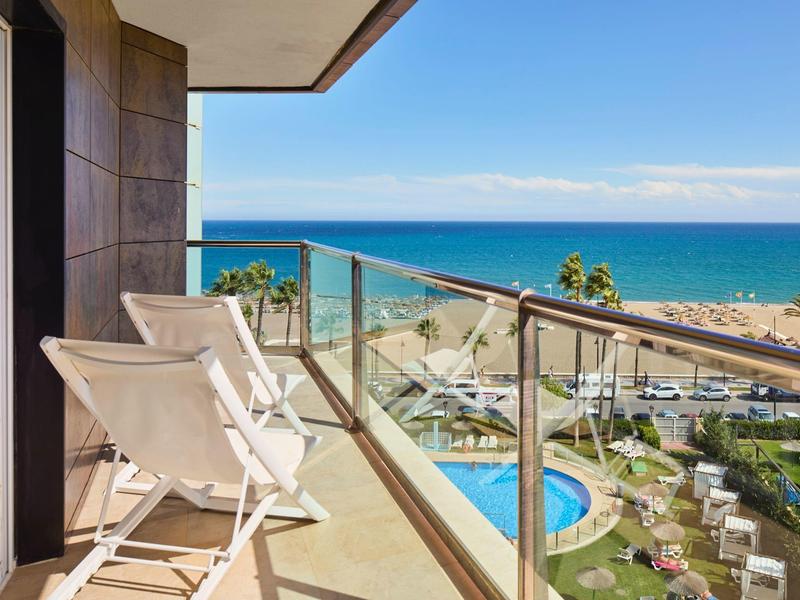 Balkon se dvěma lehátky s výhledem na moře a hotelový bazén.