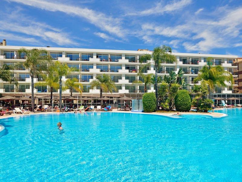 Velký hotel s velkým modrým bazénem a slunečními deštníky pod jasně modrou oblohou