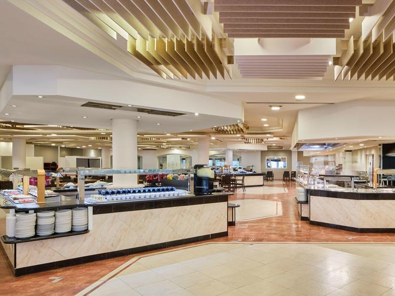 Prostorná moderní restaurace s bufetovými stanicemi a jasným stropním osvětlením.